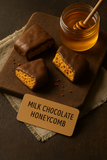 Milk chocolate honeycomb pieces on a wooden board with a jar of honey and a dipper.