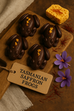 Chocolate frog candies shaped like Tasmanian saffron frogs on a wooden board with a tag.