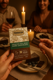 Person holding a box of Federation chocolate Dark mint chocolate with a candlelit dinner setting in the background