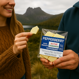 Two people holding a package of Pepperberry chocolate bars with a Cradle Mountain landscape in the background.